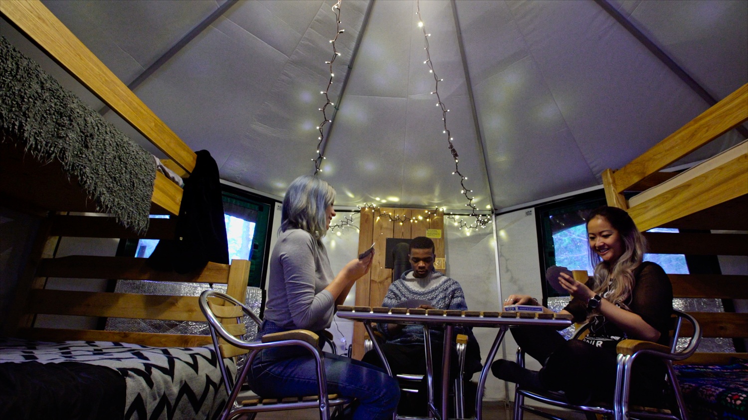 winter campers playing cards at a table inside a yurt, bunkbeds on either side