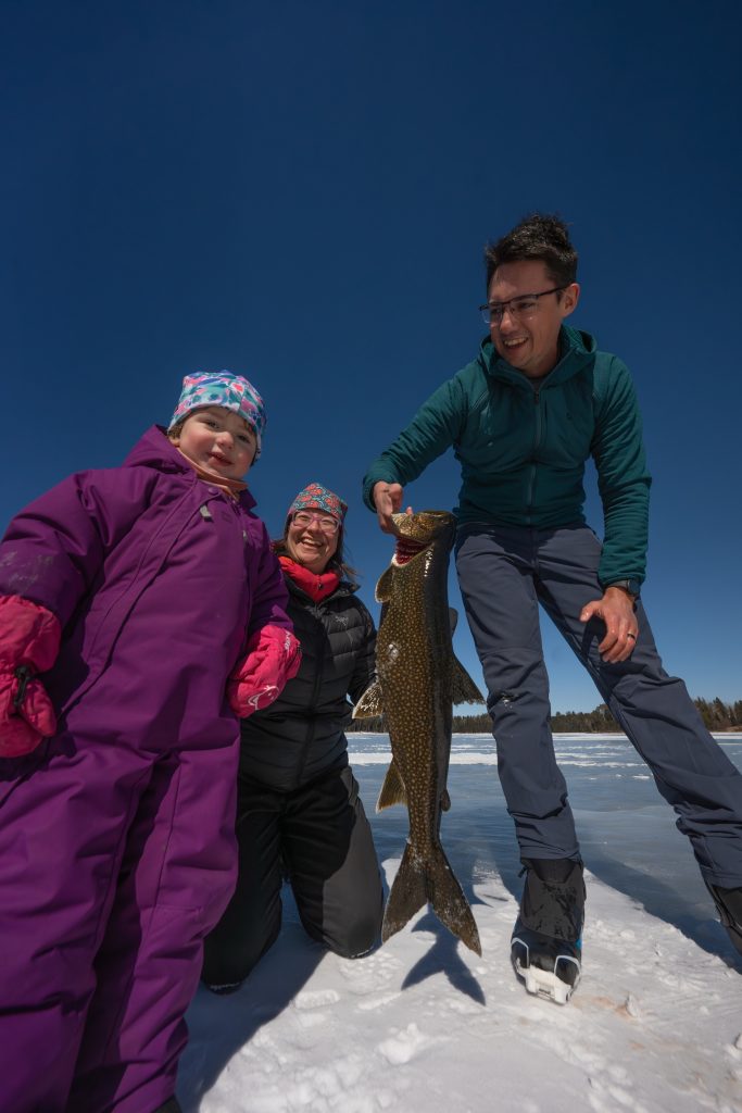 Une famille tenant une truite pêchée dans un trou creusé dans la glace