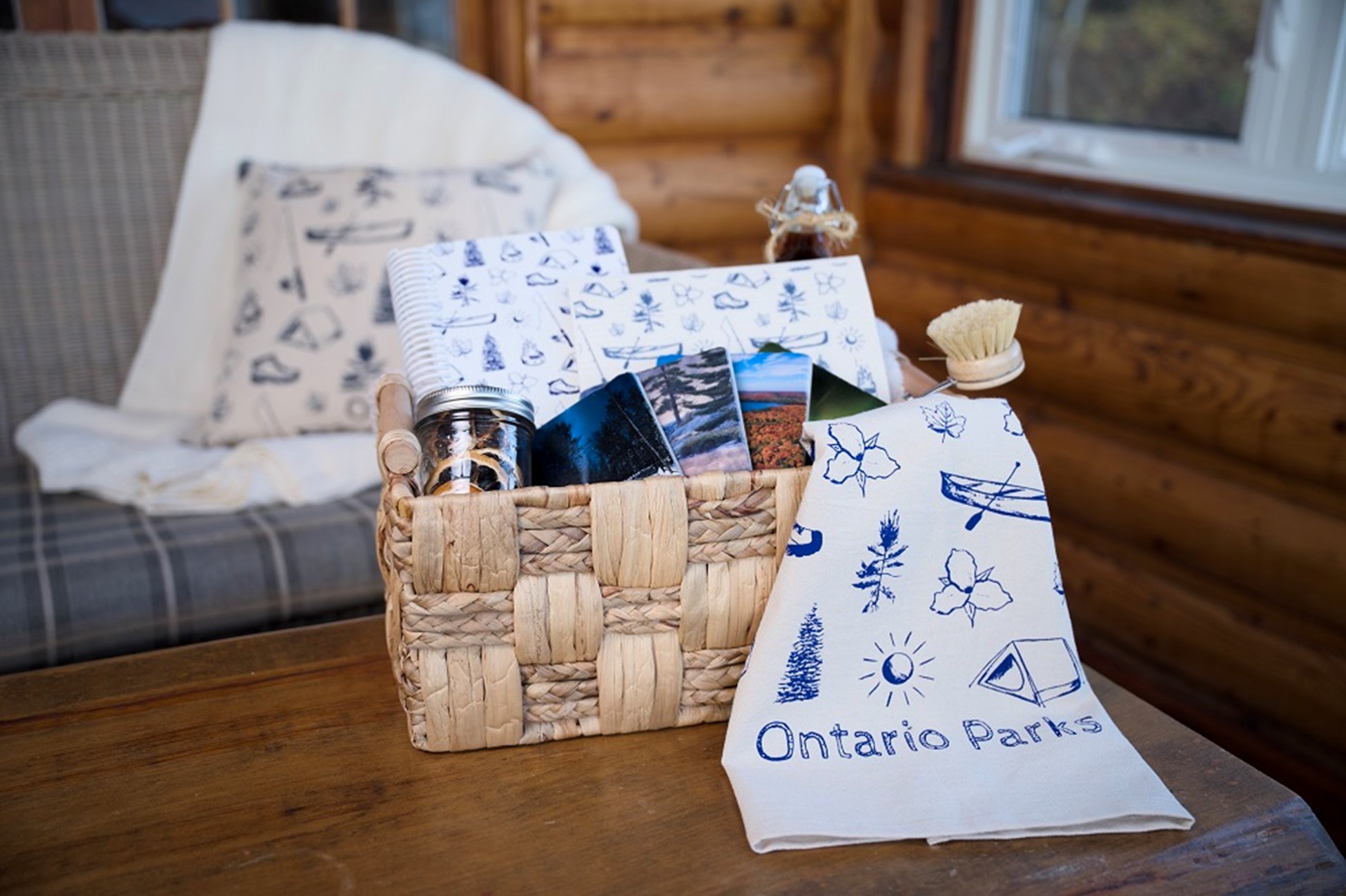 A wicker basket holding various Ontario Parks home merchandise items. The basket is on a table in a cabin with a wood interior.