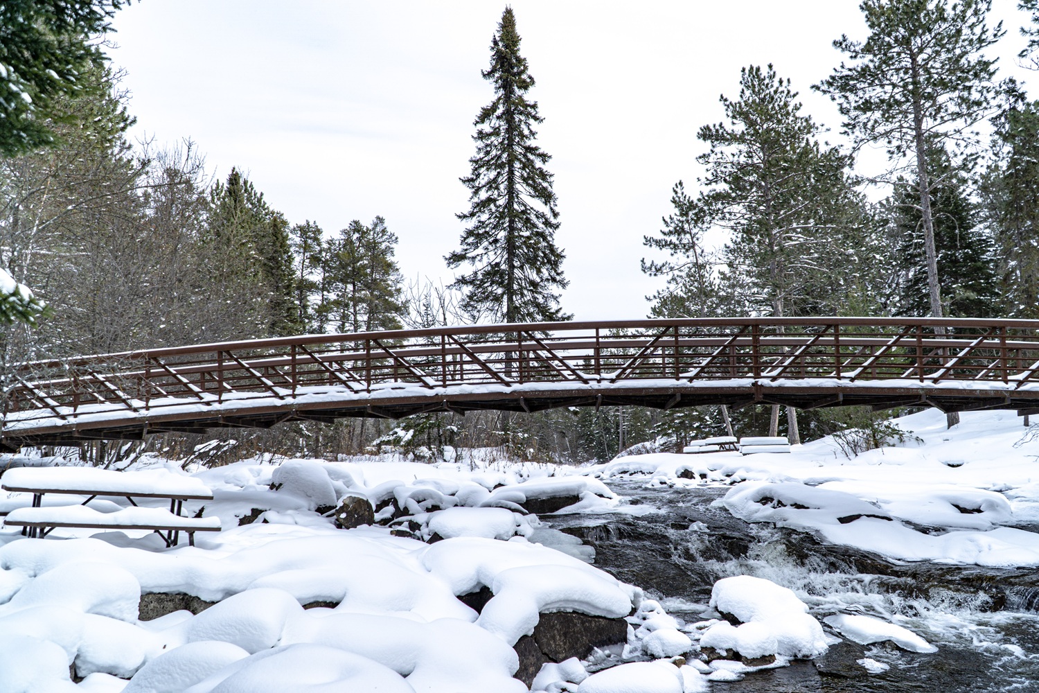 A snow covered bridge over a frozen river.