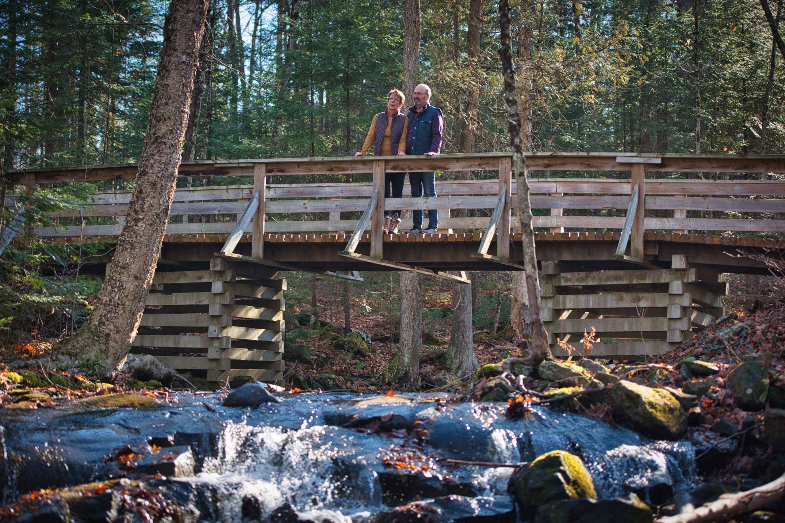 Two people stand on a wooden bridge over a creek in late fall at Silent Lake Provincial Park