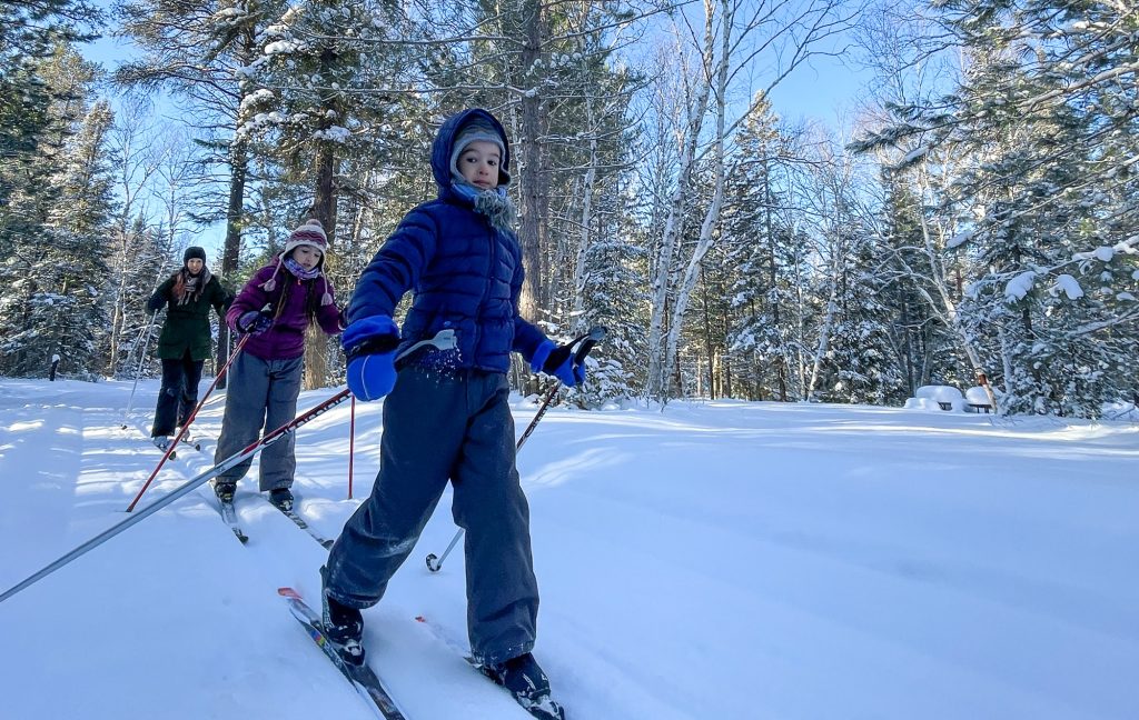children and parent cross-country skiing through forest