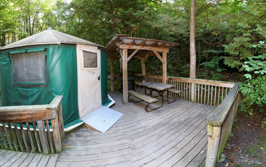 Outside of a green yurt, on wooden platform with a picnic table.