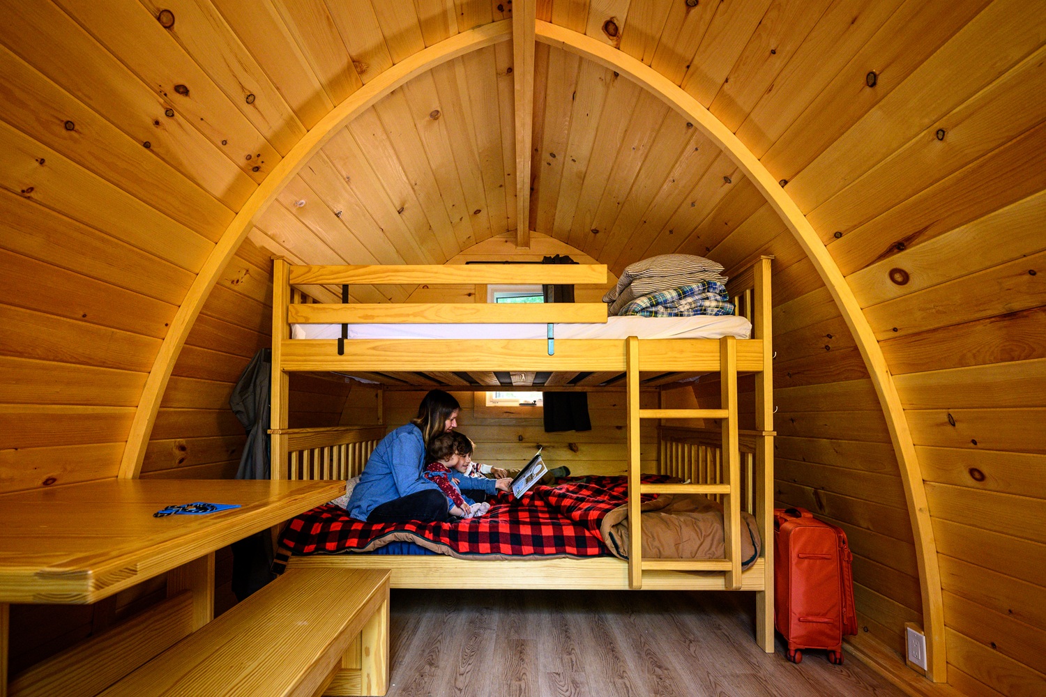 mother and children sitting on bunkbed in camping pod. Roof is wooden and rounded