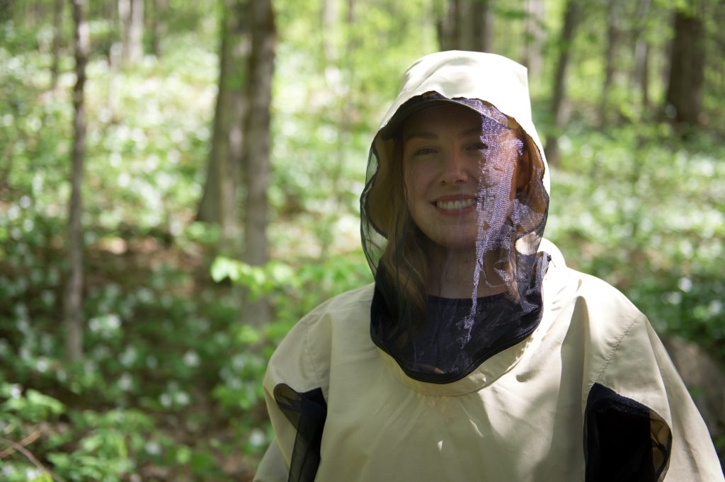 Person in bug jacket and hat, forest in background
