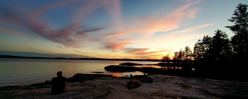 person sitting on shoreline looking at sunset