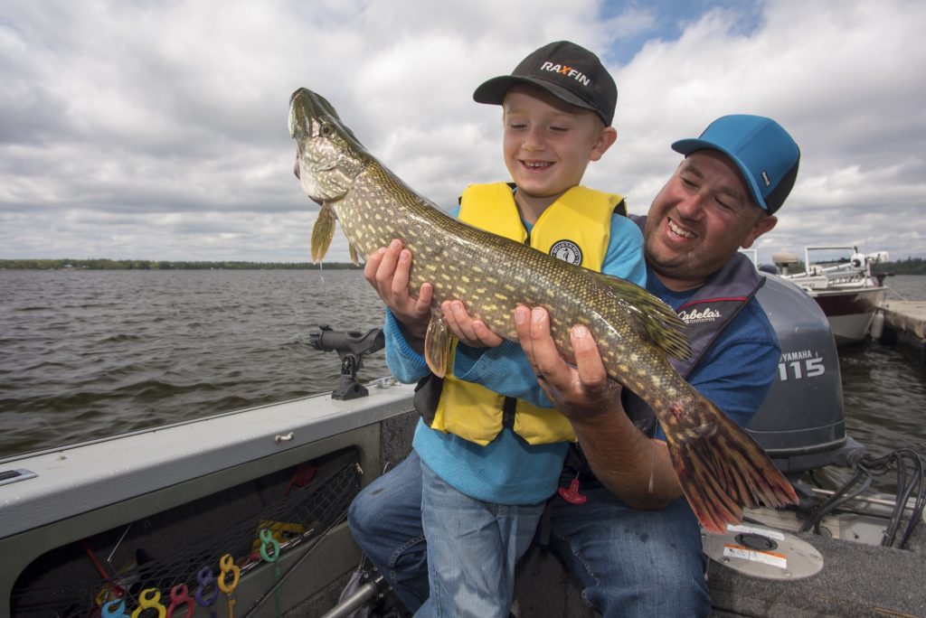father and child holding fish on boat