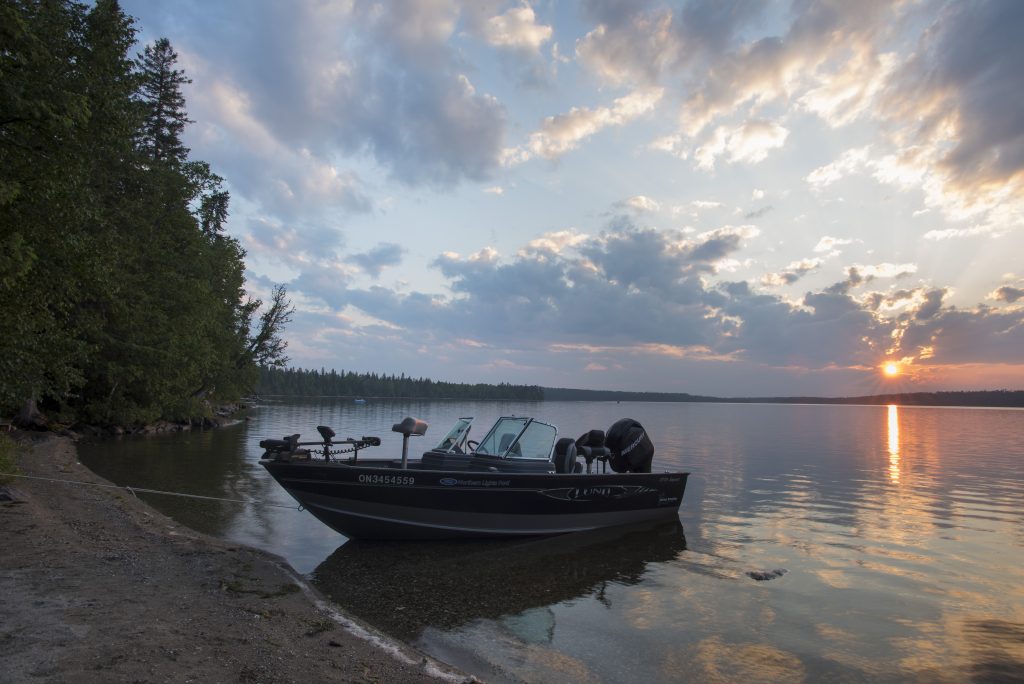 sun setting over lake. Boat docked on sandy shore