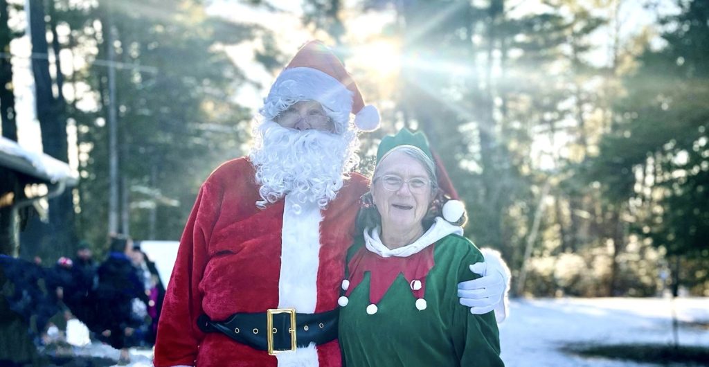 Santa arm in arm with a holiday elf in a snowy forest