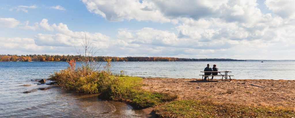 Deux personnes assises à une table de pique-nique qui regardent un lac en automne.