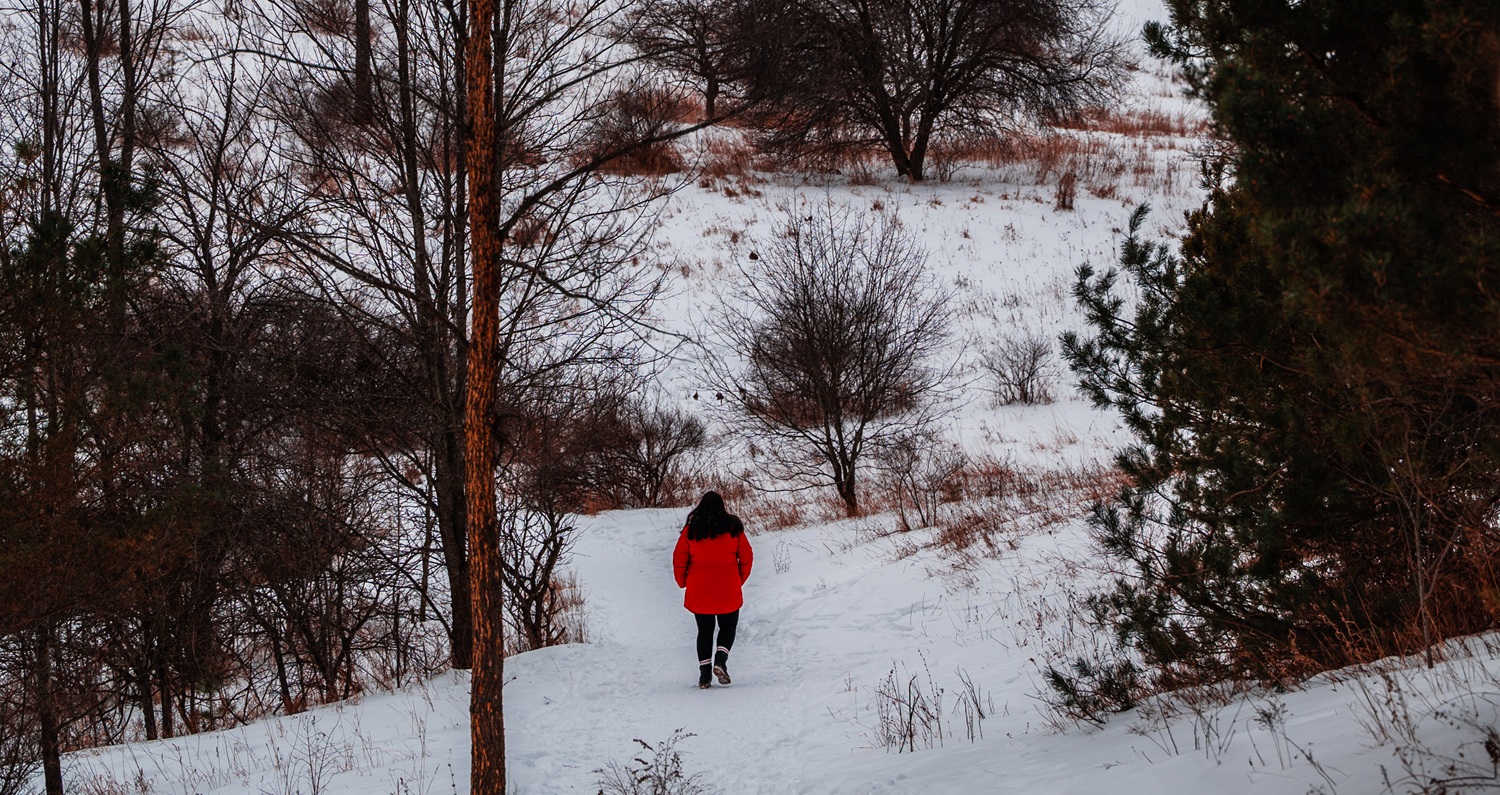 hiker on snowy trail in open field with trees