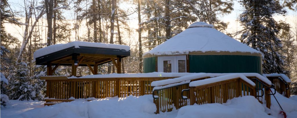 snow-covered yurt in forest at sunset