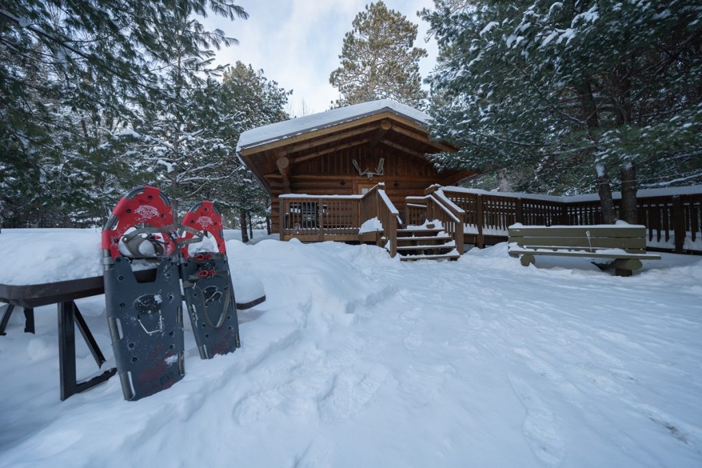 Cabane en bois rond dans une forêt enneigée avec des raquettes à l'extérieur