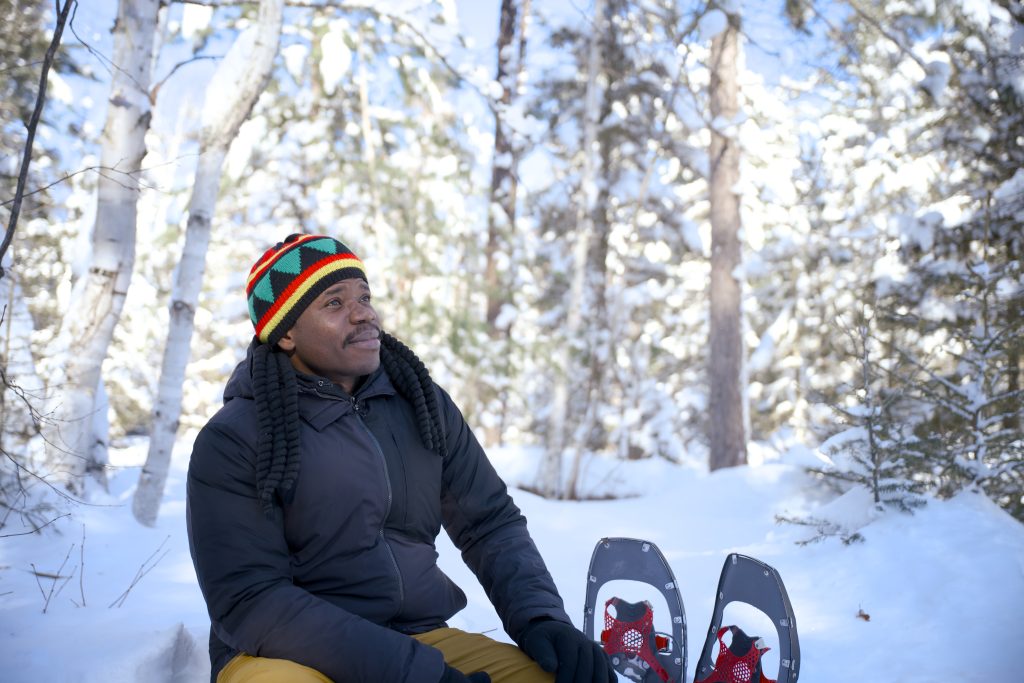 man sitting beside snowshoes, looking at snowy forest
