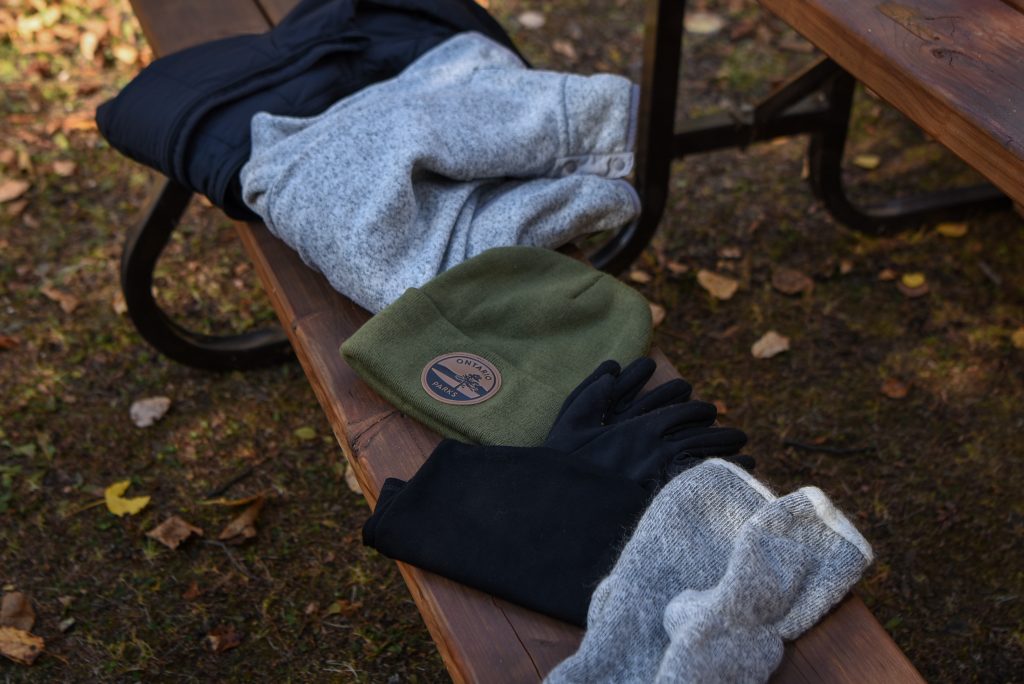 clothing including sweaters, toque, and mitts sitting on picnic table bench
