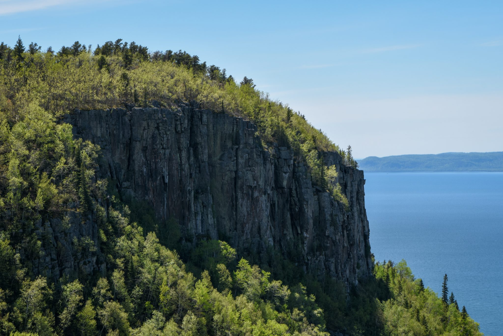 gros plan d’une falaise couverte d’arbres, devant le lac