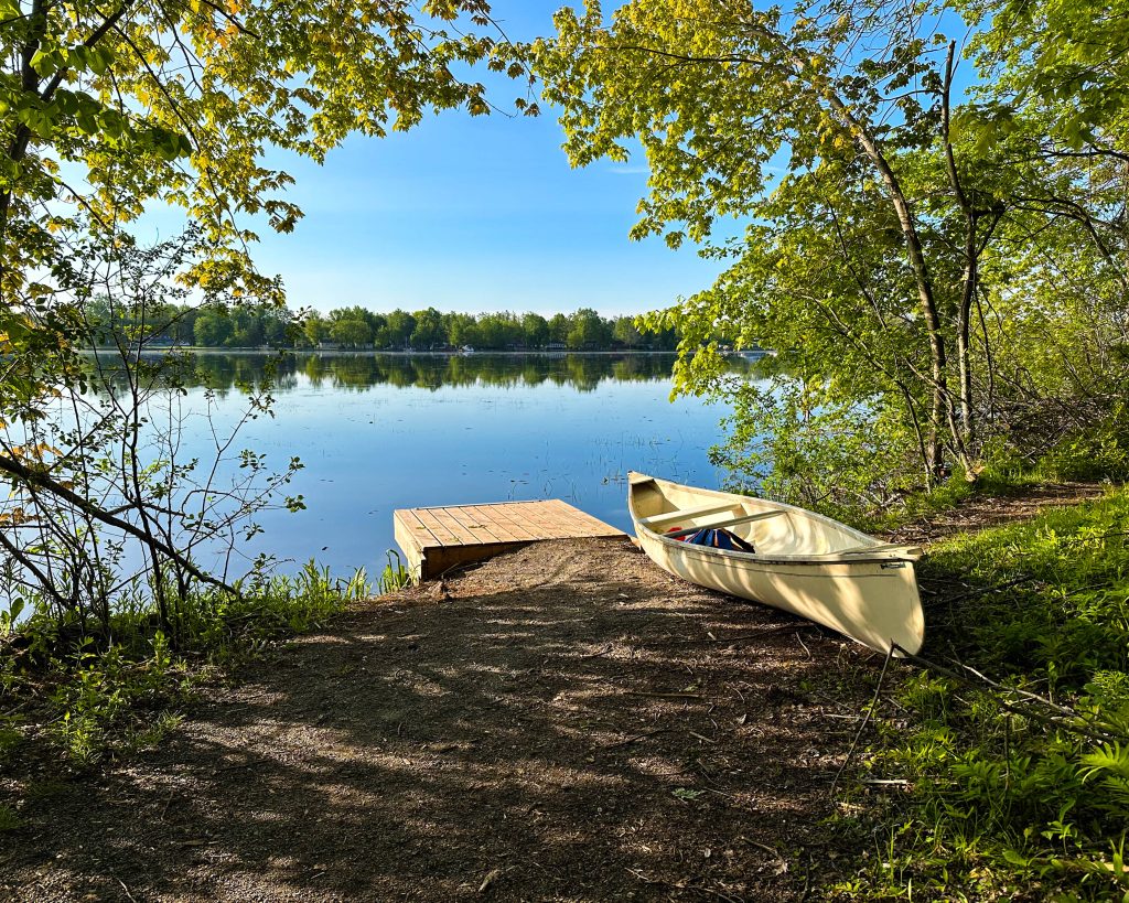 Canoe resting beside a dock on the edge of a lake. 