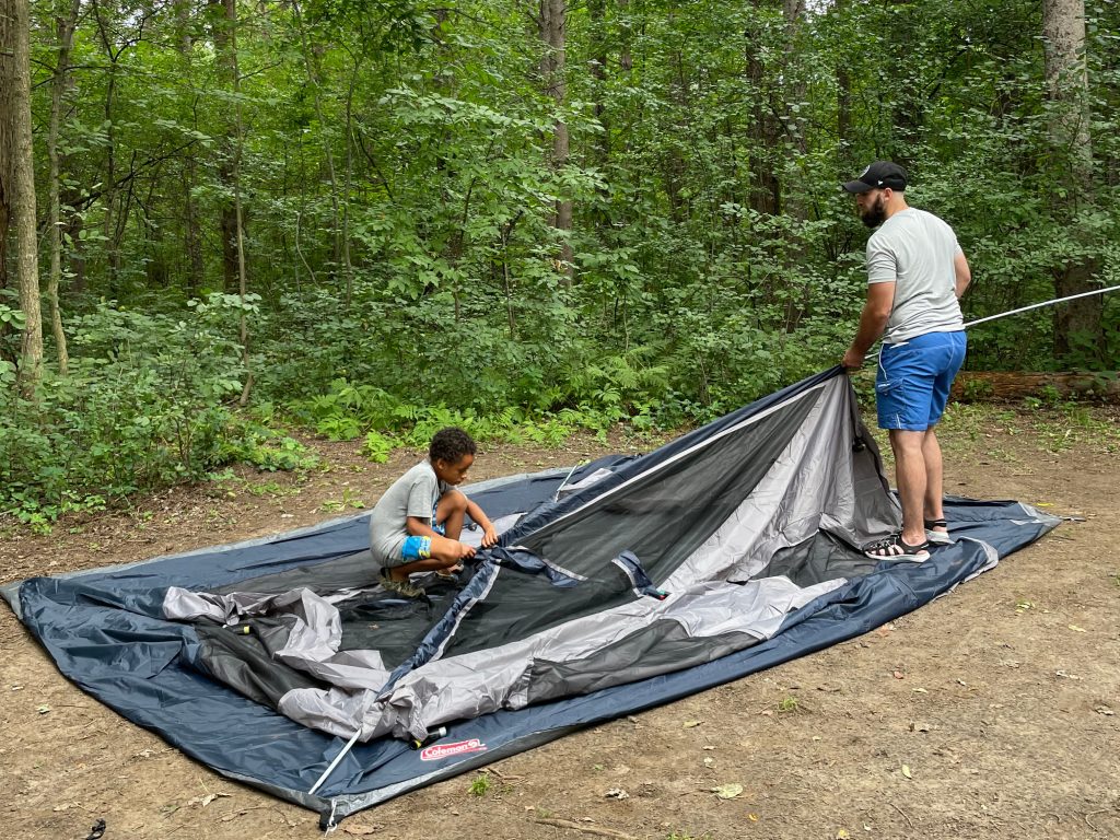 Adult and child putting a tent up in a forested campground.