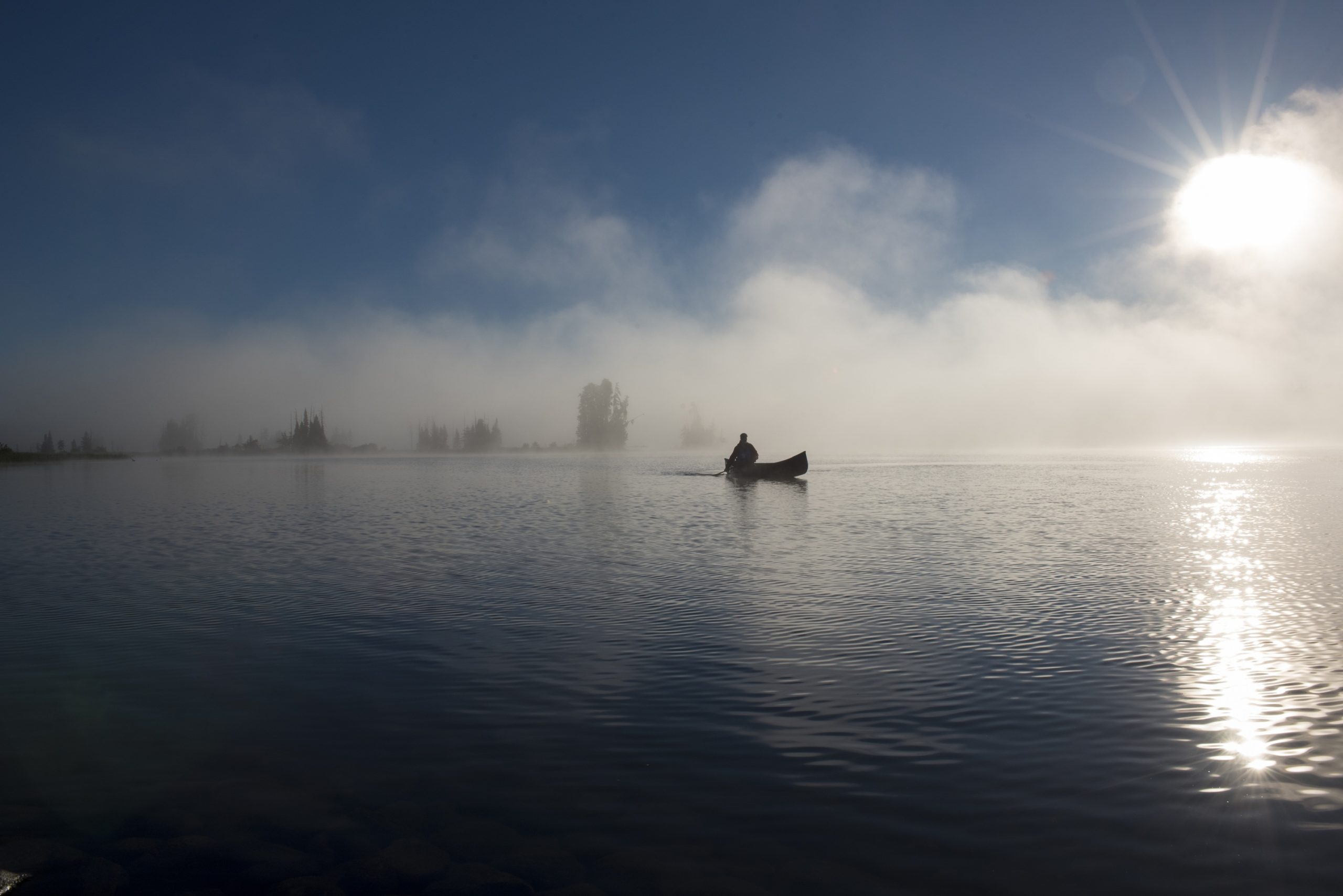 person canoeing on misty lake