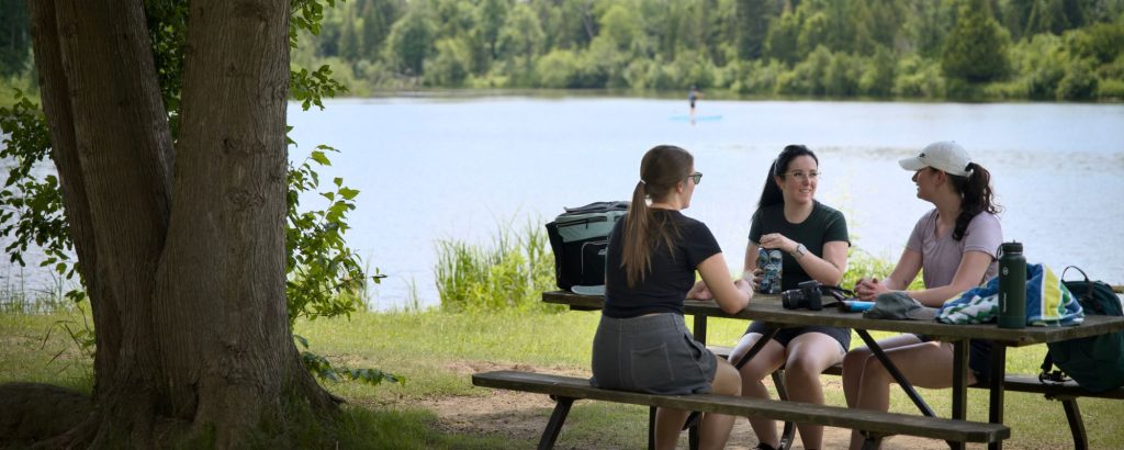 group of women sitting at picnic table on grassy shore near lake