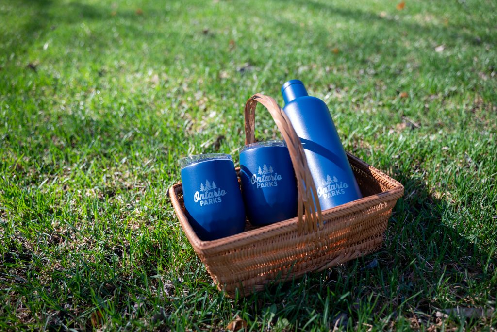 two tumblers and bottle in picnic basket sitting on grass