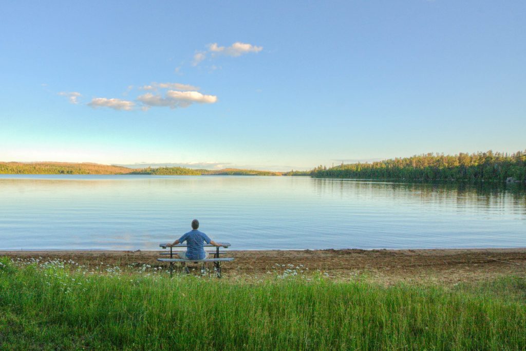 person sitting at picnic table looking out to lake 