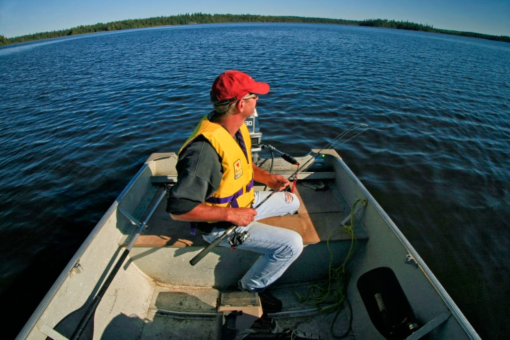 person wearing PFD sitting on boat on lake
