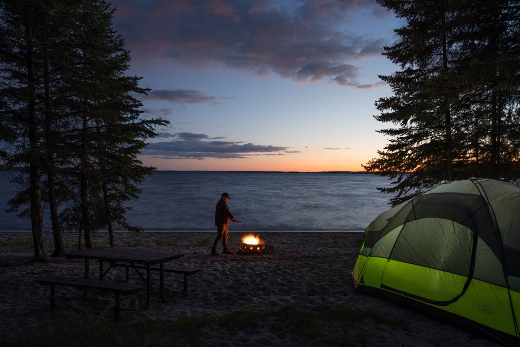 person warming up at campsite on waterfront campsite. Tent in foreground