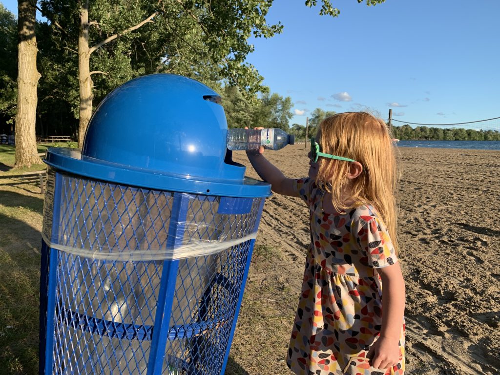 child putting plastic bottle in recycling bin on beach