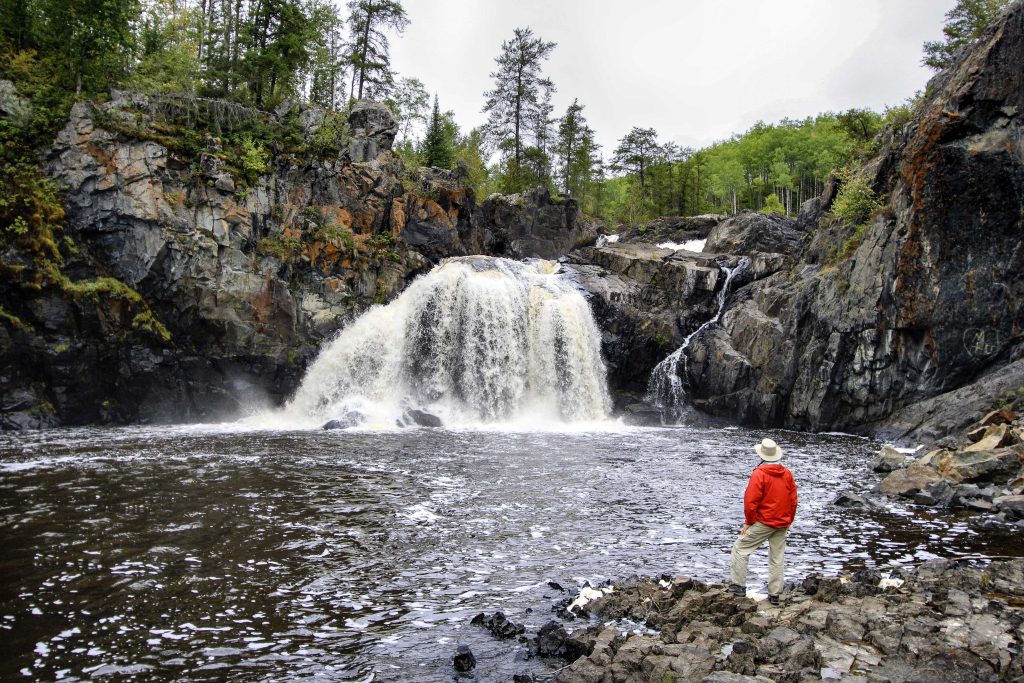 person looking up at waterfall into lake
