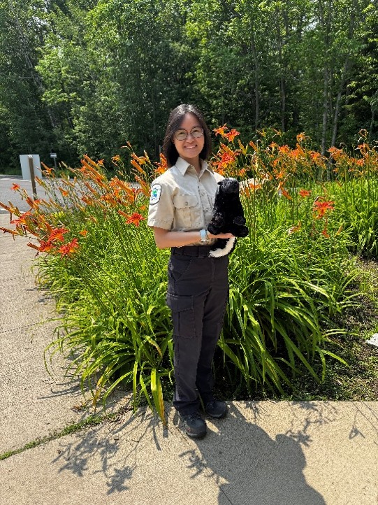 Criona holding skunk plushie, standing in front of patch of Tiger Lilies