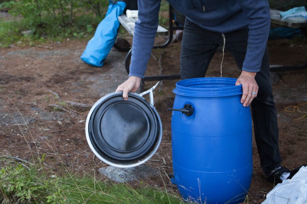 person opening up bear barrel on backcountry campsite