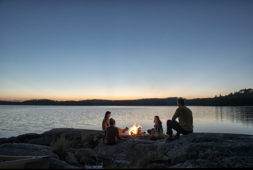 group sitting around campfire on lake's shore at twilight