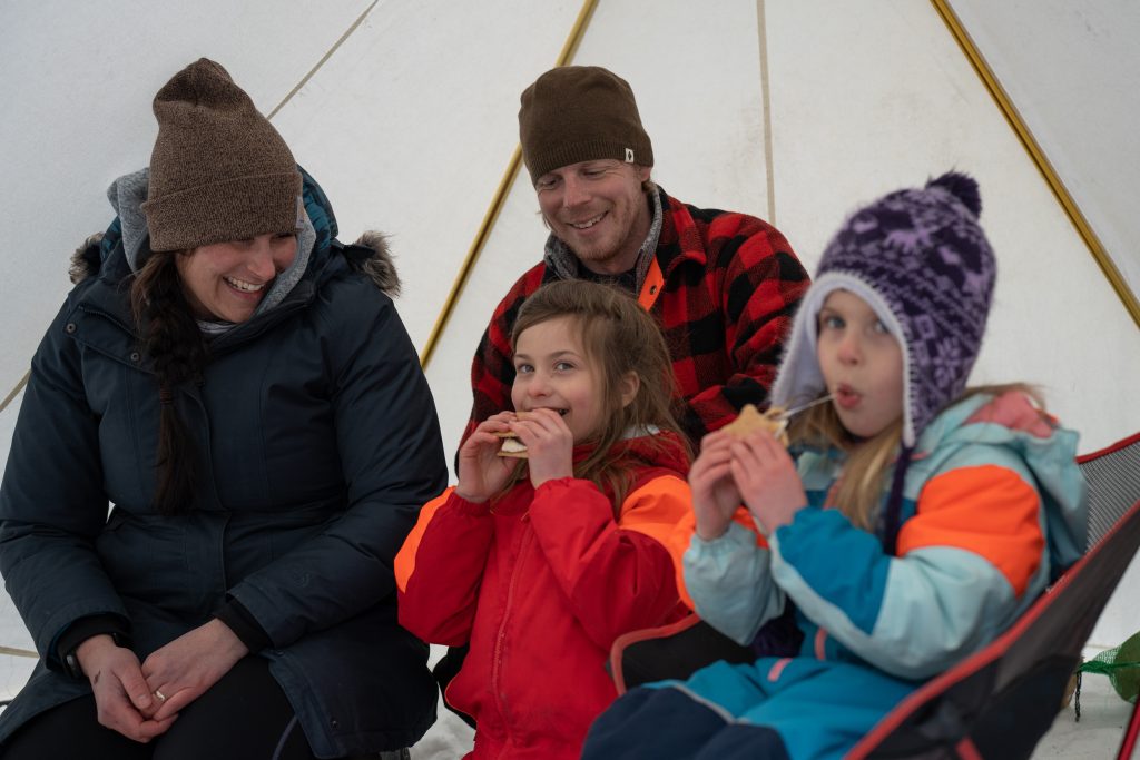 family sitting inside of hot tent, children eating s'mores