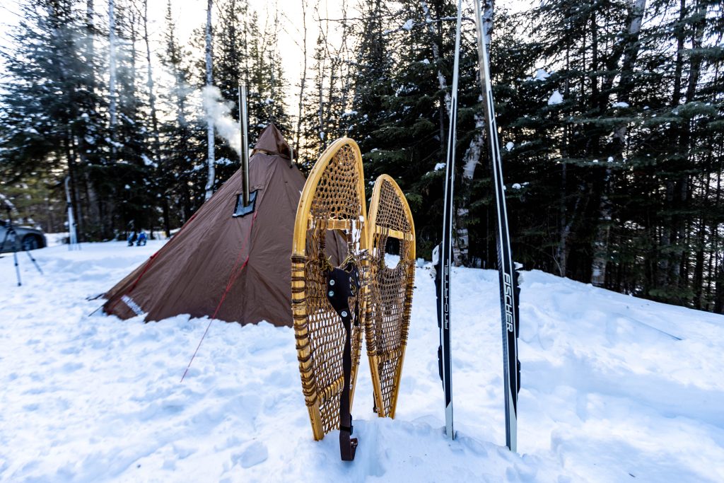 snowshoes and skis placed in snow in front of hot tent